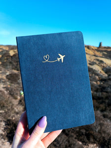A person holding a luxurious A5 Dot Grid Bullet Journal with gold foil airplane travel journal on it.