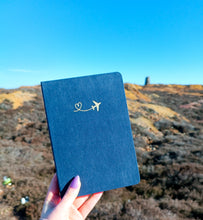 Load image into Gallery viewer, A person holding a GretelCreates Navy A5 Layflat Travel Journal with a Gold Foil Airplane design on its Brushed Velvet Cover.