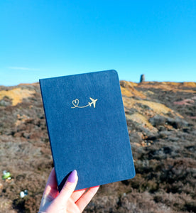 A person holding a GretelCreates Navy A5 Layflat Travel Journal with a Gold Foil Airplane design on its Brushed Velvet Cover.