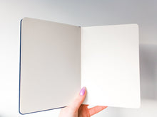 Load image into Gallery viewer, A person holding a luxurious A5 Dot Grid Bullet Journal with a brushed velvet cover on a white background.