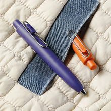 Load image into Gallery viewer, A Uni-Ball One P - Pocket Pen in Various Colours and a blue pen on top of a quilt.