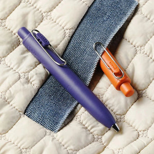 A Uni-Ball One P - Pocket Pen in Various Colours and a blue pen on top of a quilt.