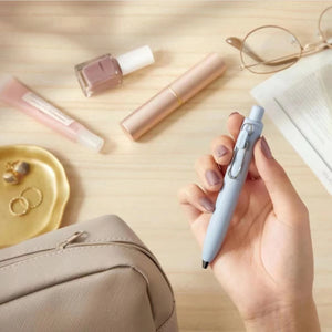 A woman is holding a Uni-Ball One P - Pocket Pen in Various Colours and a bag on a table.