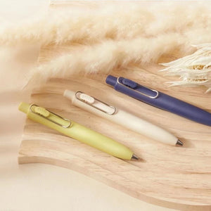 Three Uni-Ball One P - Pocket Pens in Various Colours sitting on top of a wooden board.