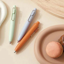 Load image into Gallery viewer, A set of uni-ball One P - Pocket Pens in various colors on a plate next to a plate of macarons.