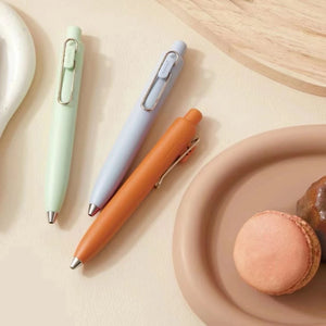 A set of uni-ball One P - Pocket Pens in various colors on a plate next to a plate of macarons.