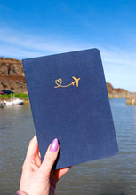 Load image into Gallery viewer, A person holding a hardback Navy A5 Dot Grid Bullet Journal with a plane on it.